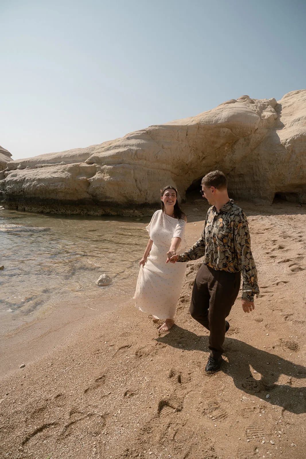 Couple walking barefoot along the shoreline below the sea caves near Peyia on the west coast of Cyprus after eloping.