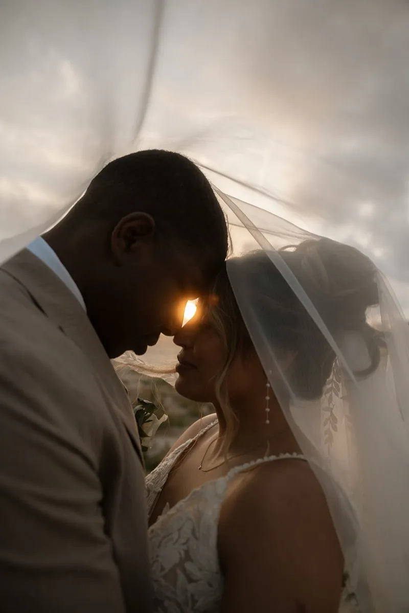 Bride and groom beneath the veil with golden sunset flare at a Cyprus wedding