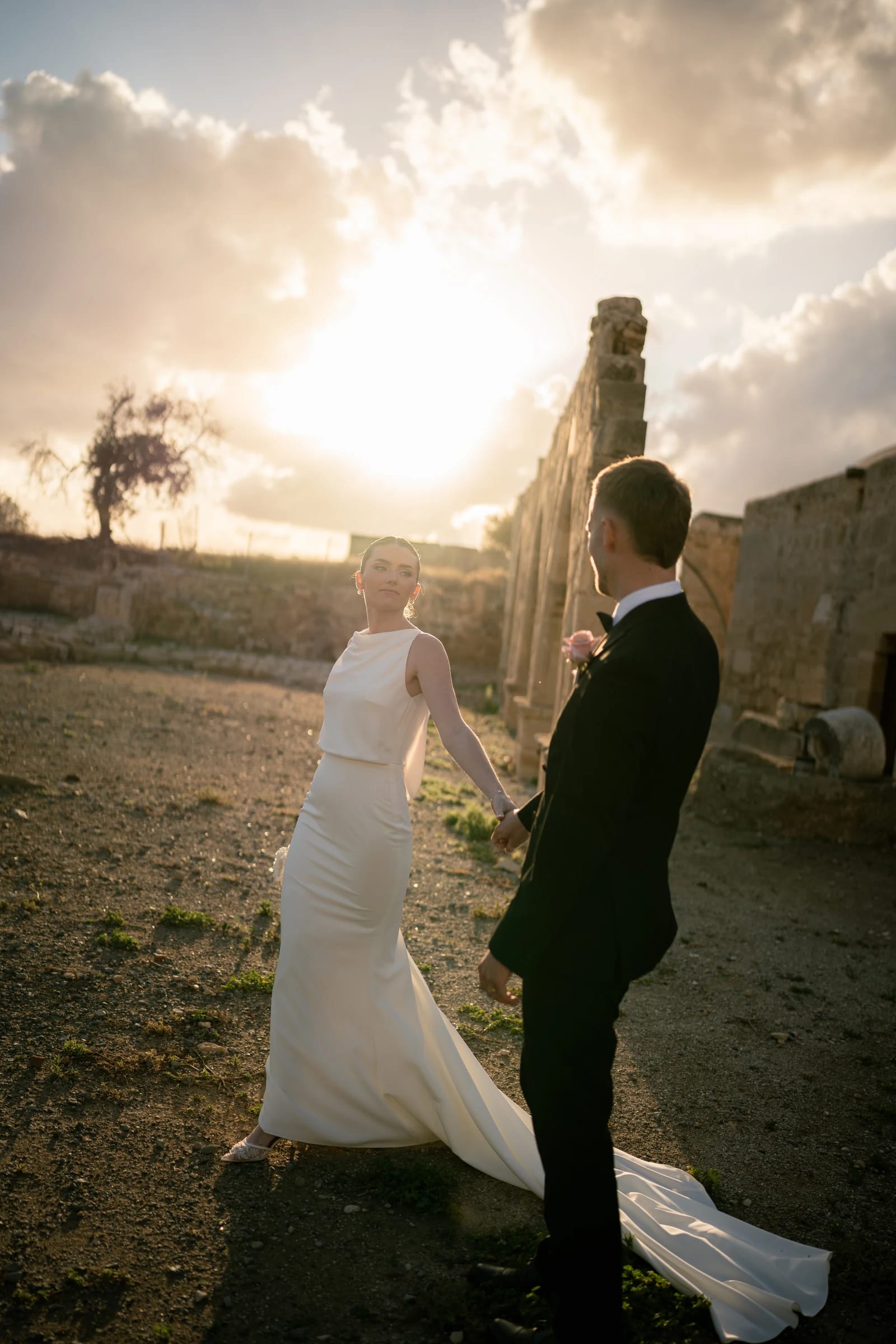 Bride and groom holding hands against a glowing sunset among the stone ruins at Liopetro, Kouklia, Paphos