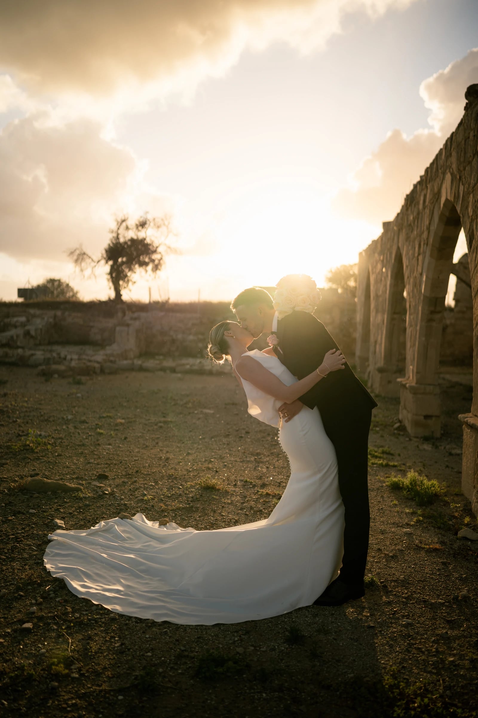 Bride and groom in a sunset dip kiss among the stone ruins at Liopetro, Kouklia, Paphos, Cyprus